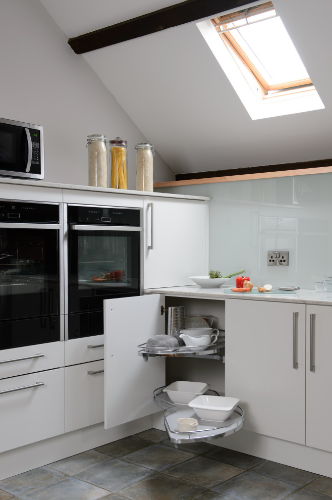 Large modern single-wall eat-in kitchen in Cornwall with a double-bowl sink, flat-panel cabinets, white cabinets, onyx benchtops, red splashback, glass sheet splashback, black appliances, cement tiles, no island, beige floor, white benchtop and exposed beam.