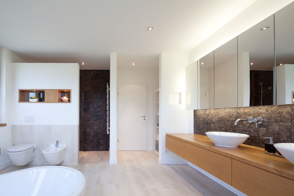 Expansive contemporary bathroom in Bremen with a vessel sink, flat-panel cabinets, light wood cabinets, wood benchtops, a freestanding tub, a wall-mount toilet, brown tile, white walls, an alcove shower, matchstick tile and brown benchtops.