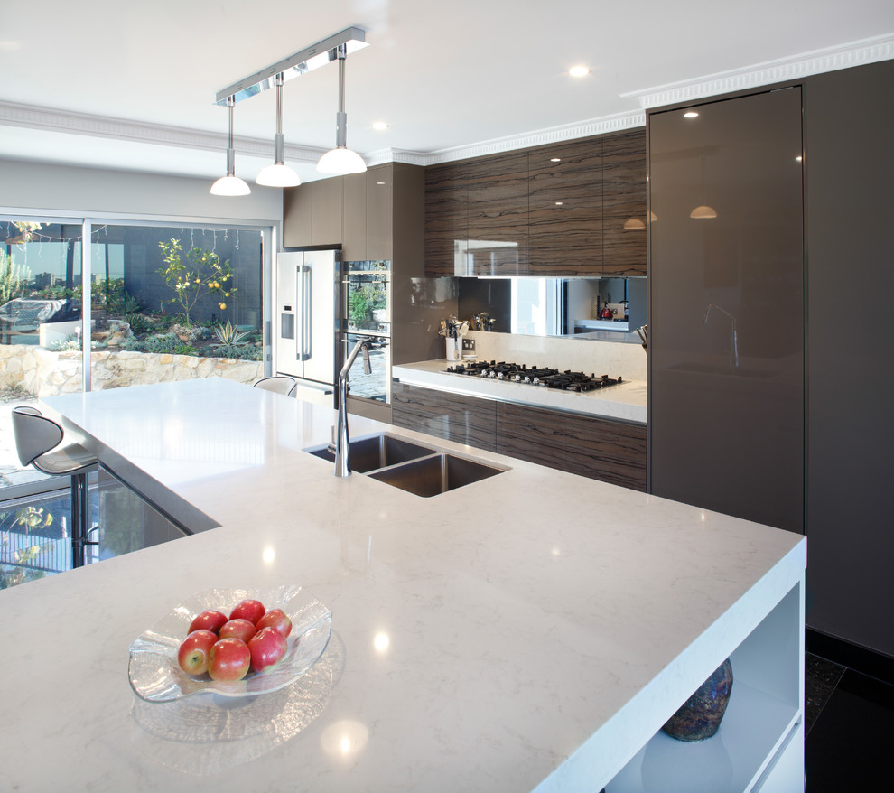 Design ideas for a large modern galley open plan kitchen in Sydney with an undermount sink, flat-panel cabinets, brown cabinets, quartz benchtops, metallic splashback, glass sheet splashback, stainless steel appliances, marble floors, with island, black floor and white benchtop.