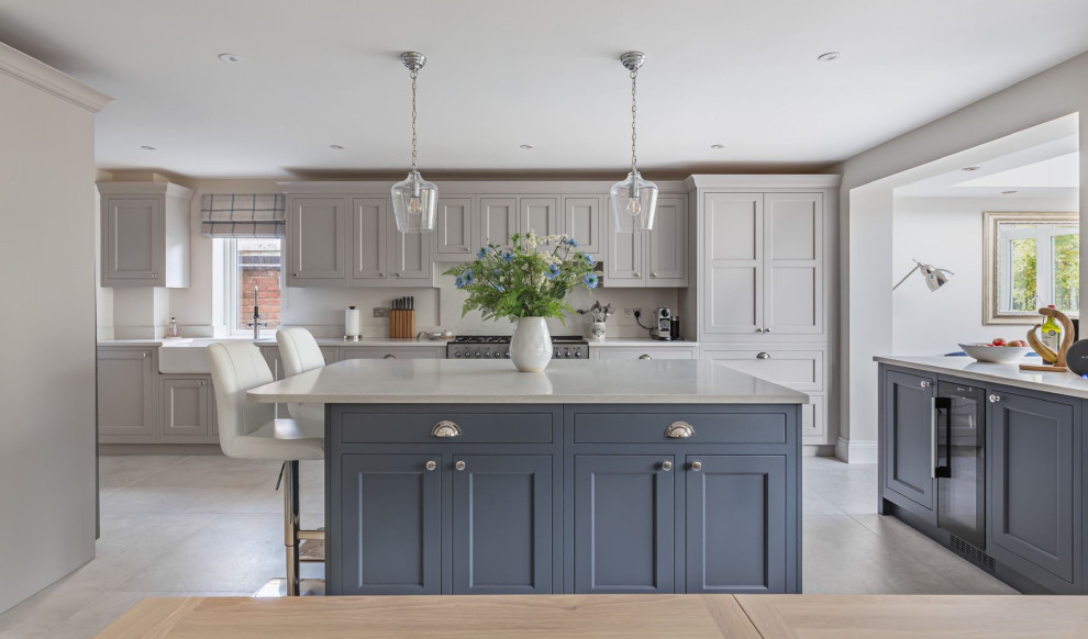 Small traditional l-shaped eat-in kitchen in Hertfordshire with a farmhouse sink, louvered cabinets, blue cabinets, quartzite benchtops, white splashback, stainless steel appliances, with island, grey floor and white benchtop.