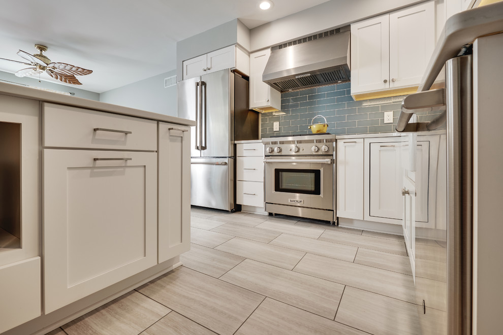 This is an example of a small modern l-shaped separate kitchen in Philadelphia with a farmhouse sink, recessed-panel cabinets, white cabinets, quartz benchtops, blue splashback, glass tile splashback, stainless steel appliances, vinyl floors, with island, beige floor and white benchtop.