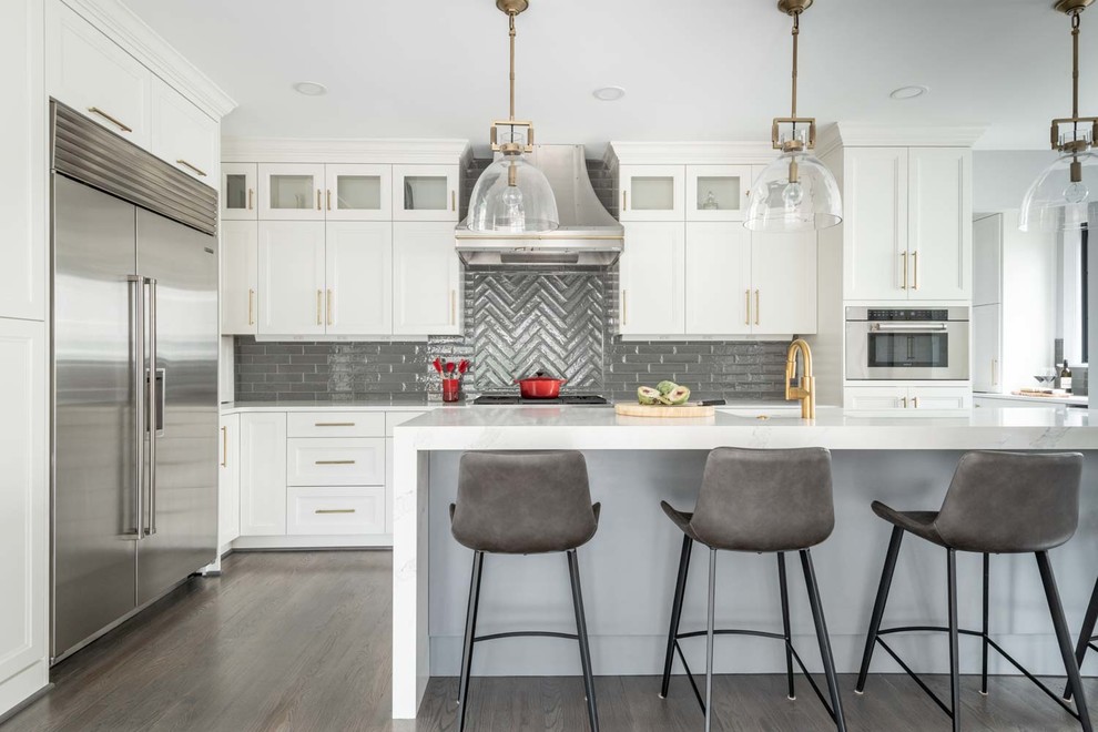 Photo of a large transitional l-shaped kitchen in DC Metro with white cabinets, grey splashback, subway tile splashback, stainless steel appliances, with island, shaker cabinets, dark hardwood floors, brown floor and grey benchtop.