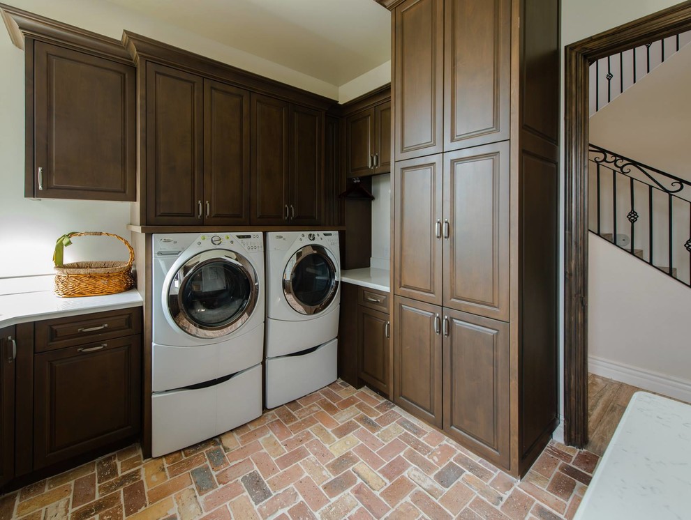 Photo of a traditional u-shaped utility room in Phoenix with raised-panel cabinets, medium wood cabinets, granite benchtops, white walls, brick floors and a side-by-side washer and dryer.