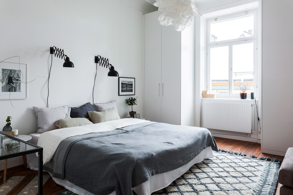 Large scandinavian master bedroom in Stockholm with white walls, dark hardwood floors and no fireplace.