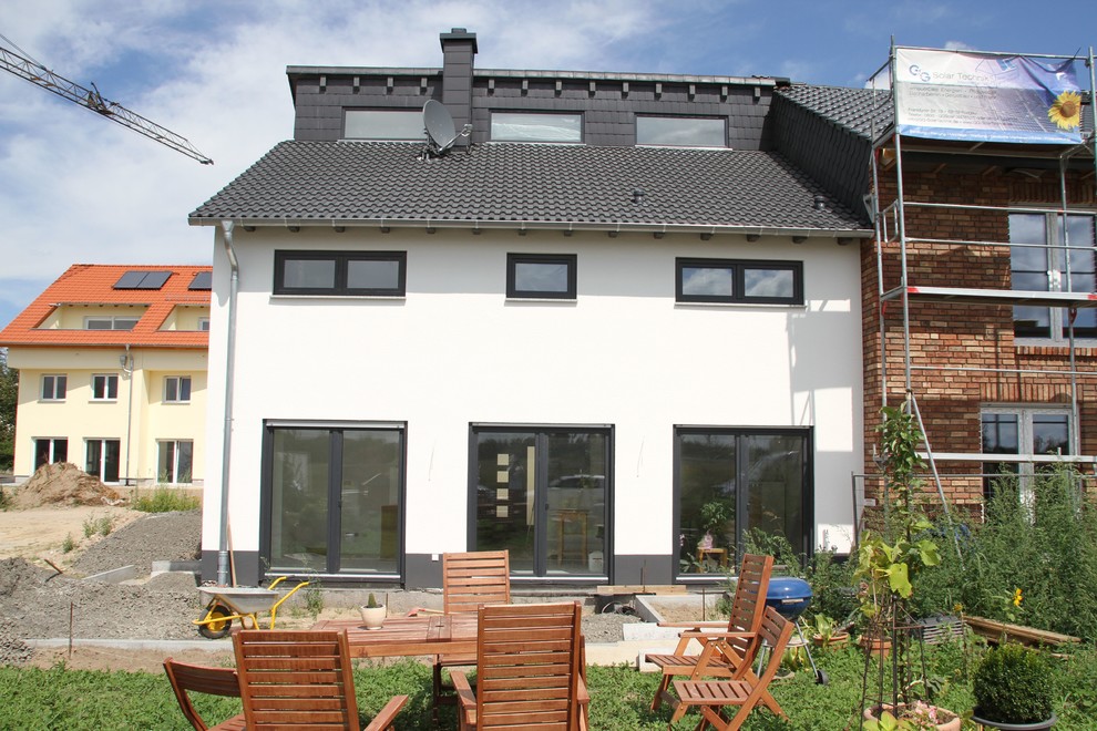 Großes, Dreistöckiges Modernes Reihenhaus mit Putzfassade, weißer Fassadenfarbe, Pultdach, Ziegeldach, schwarzem Dach und Dachgaube in Sonstige