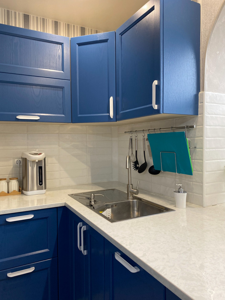 Aménagement d'une cuisine américaine classique de taille moyenne avec des portes de placard bleues, un plan de travail en quartz, une crédence blanche, aucun îlot, un sol marron et un plan de travail blanc.