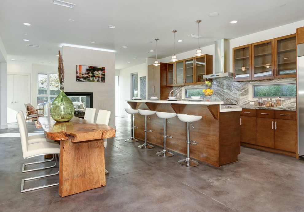 Photo of a mid-sized contemporary single-wall eat-in kitchen in Los Angeles with a double-bowl sink, glass-front cabinets, medium wood cabinets, granite benchtops, white splashback, stainless steel appliances, concrete floors, with island and stone slab splashback.