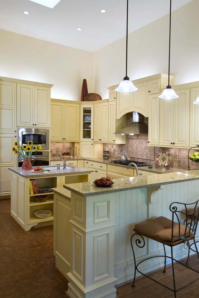 Photo of an arts and crafts u-shaped eat-in kitchen in Other with an undermount sink, raised-panel cabinets, white cabinets, beige splashback, ceramic splashback, stainless steel appliances, cork floors and with island.