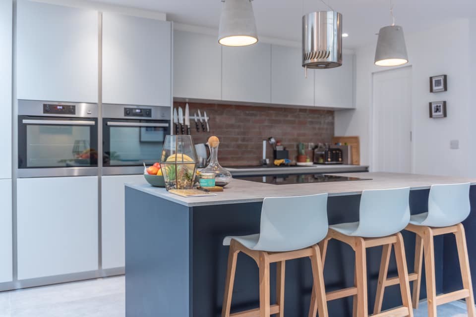 Mid-sized modern single-wall eat-in kitchen in Cardiff with an integrated sink, flat-panel cabinets, blue cabinets, concrete benchtops, red splashback, brick splashback, stainless steel appliances, concrete floors, with island, grey floor and grey benchtop.
