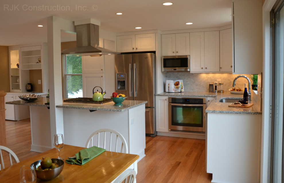 Inspiration for an expansive transitional l-shaped open plan kitchen in DC Metro with an undermount sink, shaker cabinets, white cabinets, granite benchtops, grey splashback, ceramic splashback, stainless steel appliances, light hardwood floors and with island.