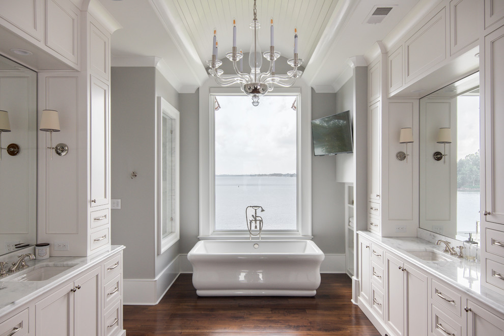 Inspiration for a traditional master bathroom in Charlotte with recessed-panel cabinets, beige cabinets, a freestanding tub, grey walls, medium hardwood floors and an undermount sink.