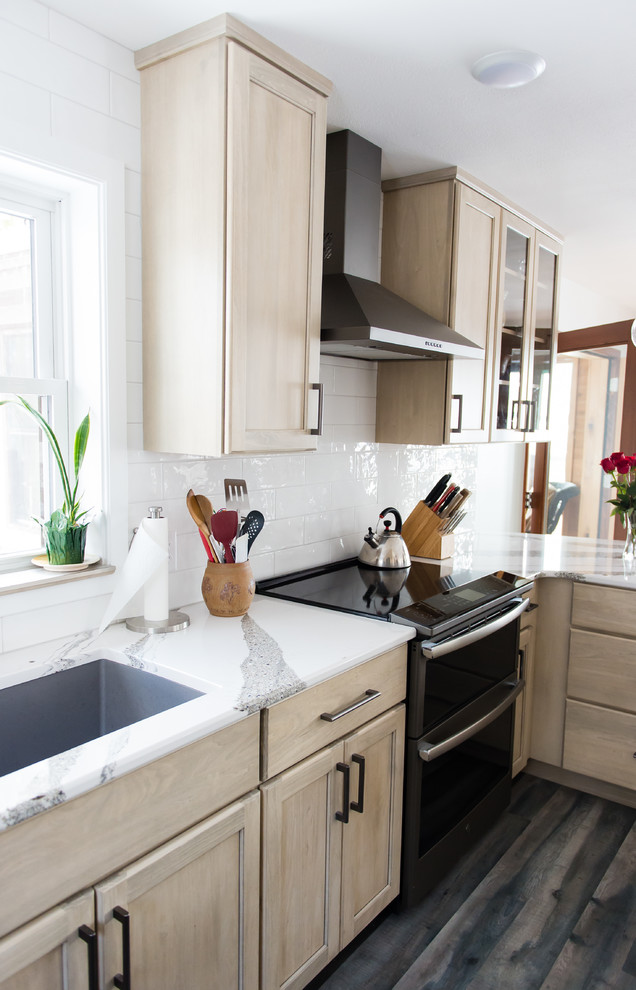 Mid-sized transitional u-shaped vinyl floor and brown floor enclosed kitchen photo with an undermount sink, flat-panel cabinets, beige cabinets, quartz countertops, white backsplash, subway tile backsplash, black appliances, a peninsula and white countertops