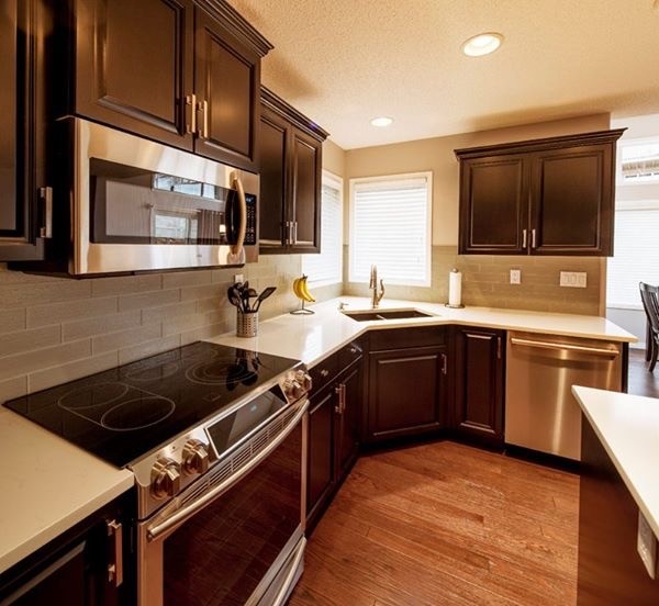 Example of a large transitional u-shaped dark wood floor and brown floor eat-in kitchen design in Calgary with a double-bowl sink, raised-panel cabinets, dark wood cabinets, quartz countertops, gray backsplash, ceramic backsplash, stainless steel appliances and an island