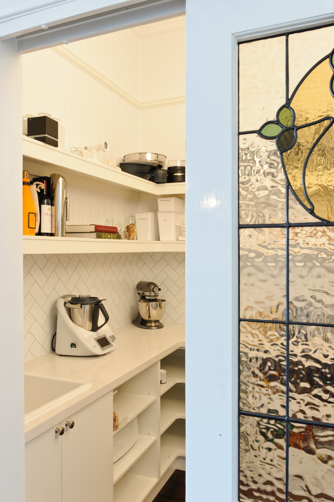 This is an example of a small traditional kitchen pantry in Brisbane with open cabinets, white cabinets, white splashback, porcelain splashback, dark hardwood floors and with island.