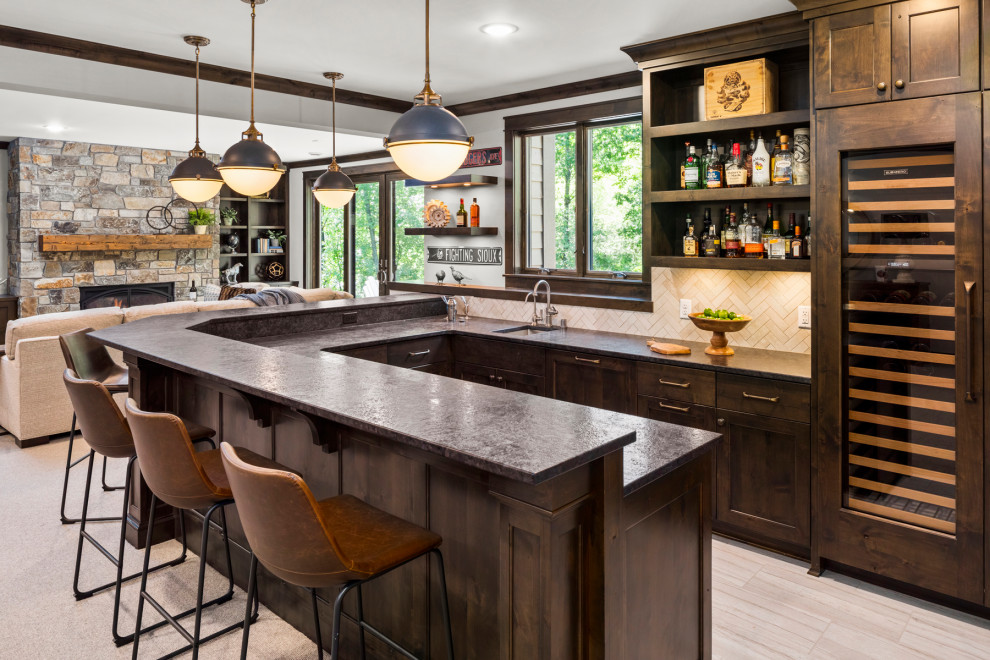 Photo of a mid-sized traditional u-shaped seated home bar in Minneapolis with an undermount sink, flat-panel cabinets, brown cabinets, beige splashback, ceramic splashback, ceramic floors, beige floor and black benchtop.