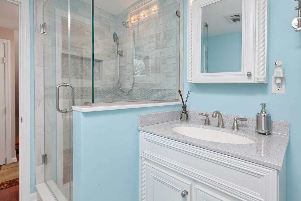 This is an example of a mid-sized beach style 3/4 bathroom in Philadelphia with white cabinets, a corner shower, a two-piece toilet, multi-coloured tile, ceramic tile, blue walls, ceramic floors, an undermount sink, glass benchtops and recessed-panel cabinets.