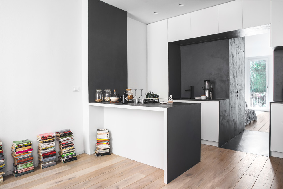 Photo of a small contemporary galley open plan kitchen in Bologna with a single-bowl sink, flat-panel cabinets, white cabinets, wood benchtops, grey splashback, black appliances, light hardwood floors, with island and brown floor.