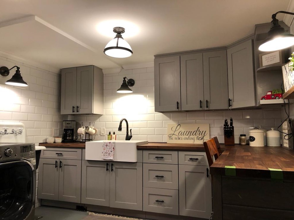 Mid-sized country l-shaped dedicated laundry room in Denver with a farmhouse sink, shaker cabinets, grey cabinets, wood benchtops, white walls, a side-by-side washer and dryer and brown benchtop.