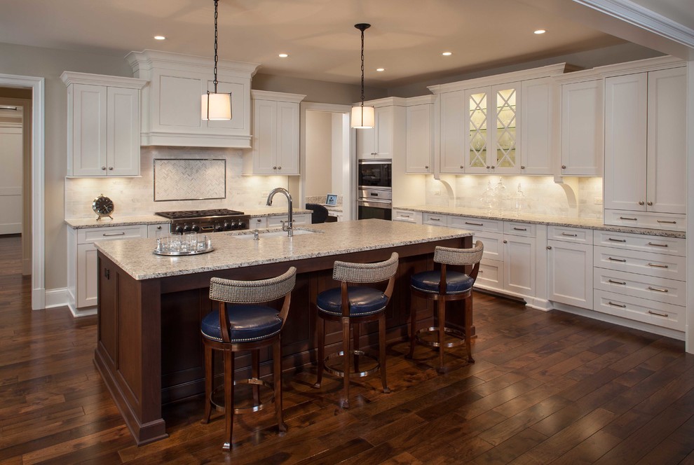 Design ideas for a mid-sized transitional l-shaped open plan kitchen in Chicago with an undermount sink, recessed-panel cabinets, white cabinets, granite benchtops, white splashback, ceramic splashback, stainless steel appliances, dark hardwood floors, with island and brown floor.