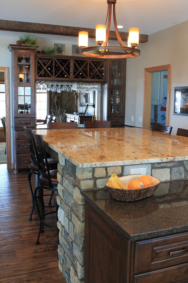 Mid-sized mountain style u-shaped medium tone wood floor kitchen photo with raised-panel cabinets, dark wood cabinets, granite countertops, beige backsplash, ceramic backsplash, black appliances and an island