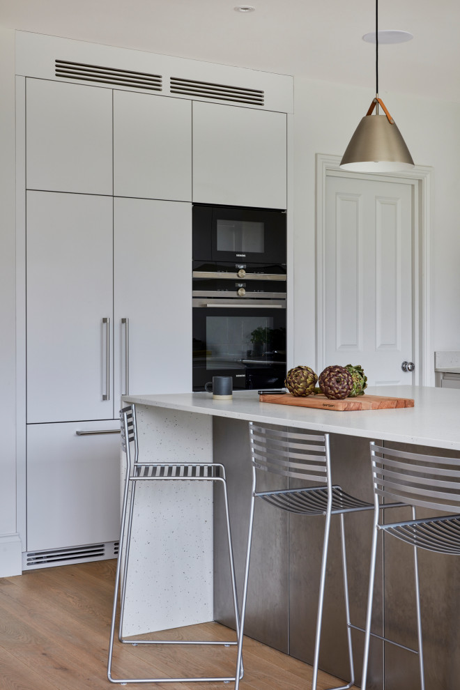 Bild på ett stort skandinaviskt vit vitt kök och matrum, med släta luckor, vita skåp, bänkskiva i koppar, vitt stänkskydd, svarta vitvaror och en köksö