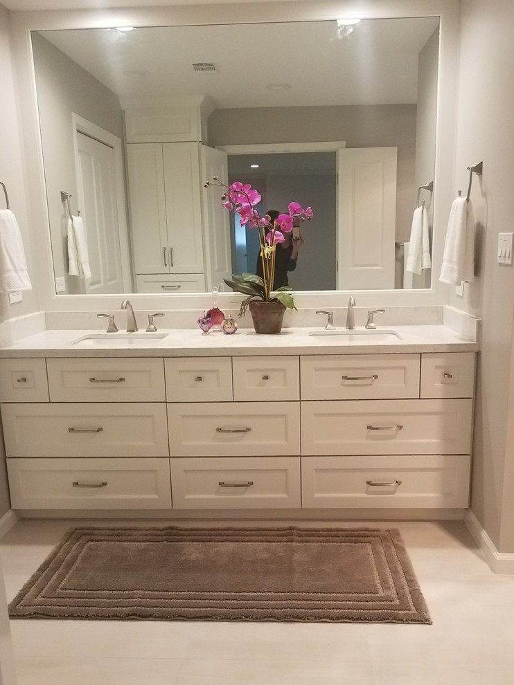 Photo of a large transitional master bathroom in Houston with recessed-panel cabinets, white cabinets, a curbless shower, a one-piece toilet, gray tile, porcelain tile, grey walls, porcelain floors, an undermount sink, engineered quartz benchtops, white floor and a hinged shower door.