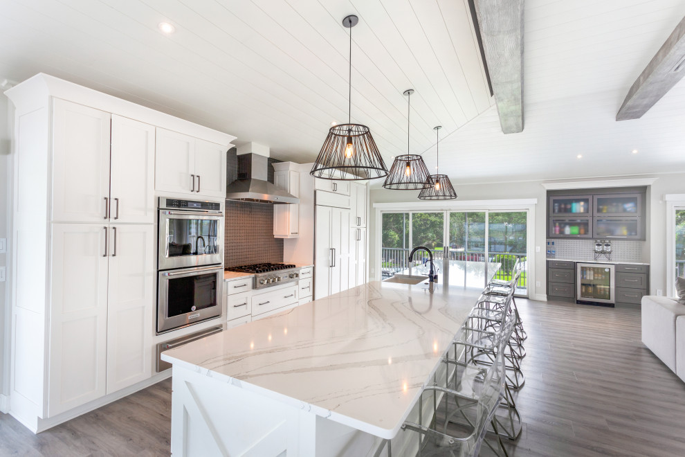 Photo of an expansive beach style single-wall eat-in kitchen in Jacksonville with a farmhouse sink, shaker cabinets, white cabinets, quartz benchtops, black splashback, glass sheet splashback, stainless steel appliances, vinyl floors, with island, multi-coloured floor, multi-coloured benchtop and exposed beam.