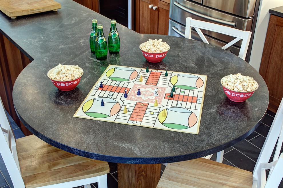 Example of a mid-sized minimalist u-shaped slate floor eat-in kitchen design in New York with a farmhouse sink, shaker cabinets, medium tone wood cabinets, granite countertops, green backsplash, glass tile backsplash, stainless steel appliances and an island