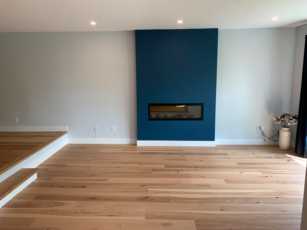 Design ideas for a mid-sized contemporary open concept living room in Vancouver with blue walls, light hardwood floors, a standard fireplace, a plaster fireplace surround and multi-coloured floor.