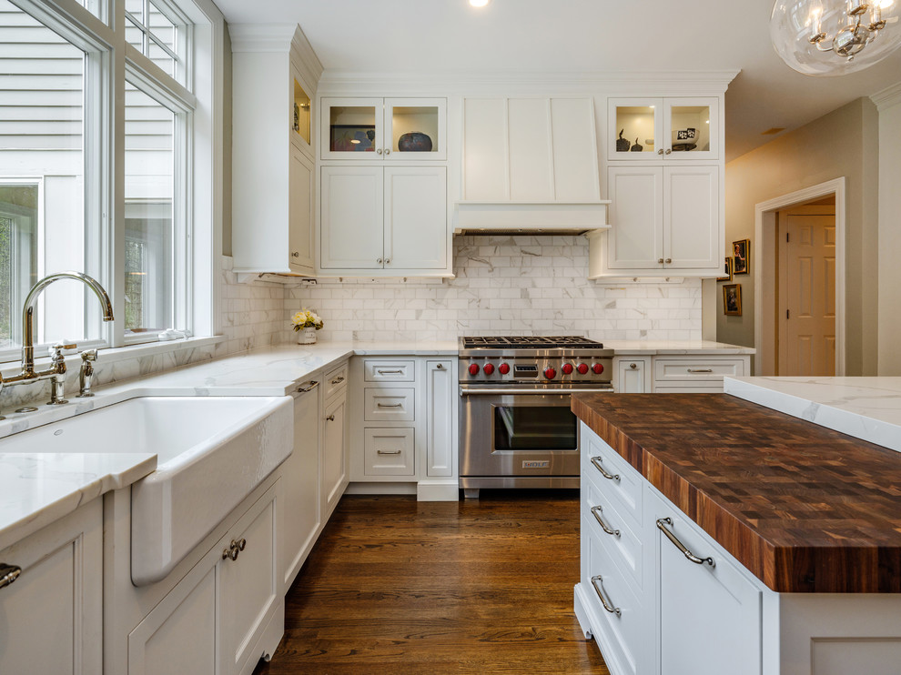 Example of a large transitional u-shaped dark wood floor and brown floor kitchen design in Bridgeport with a farmhouse sink, flat-panel cabinets, white cabinets, quartz countertops, white backsplash, marble backsplash, stainless steel appliances, an island and white countertops