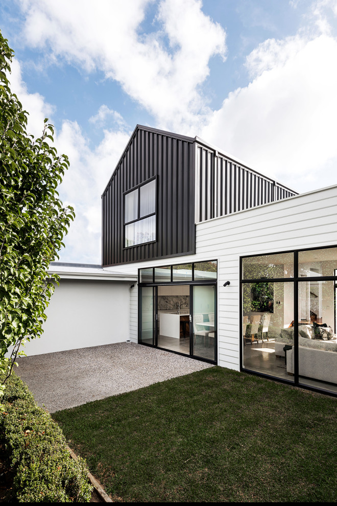 Idée de décoration pour une petite façade de maison métallique et blanche minimaliste en planches et couvre-joints à un étage avec un toit en appentis, un toit en métal et un toit noir.
