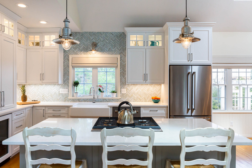 Example of a mid-sized beach style l-shaped medium tone wood floor, brown floor and vaulted ceiling eat-in kitchen design in Boston with an undermount sink, shaker cabinets, white cabinets, quartz countertops, blue backsplash, glass tile backsplash, stainless steel appliances, an island and white countertops