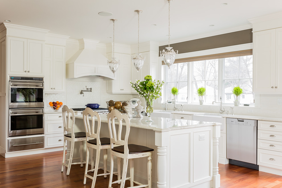Large traditional l-shaped eat-in kitchen in Boston with a farmhouse sink, white cabinets, quartzite benchtops, white splashback, white appliances, dark hardwood floors and with island.