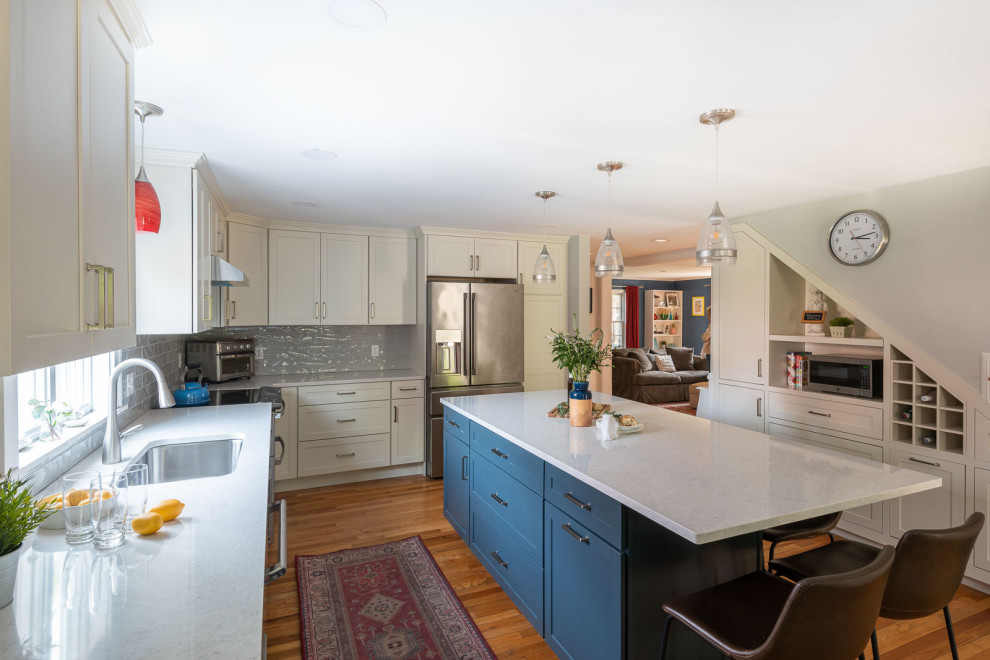 Inspiration for a large transitional l-shaped light wood floor and brown floor eat-in kitchen remodel in Boston with an undermount sink, shaker cabinets, white cabinets, quartz countertops, gray backsplash, ceramic backsplash, stainless steel appliances, an island and white countertops