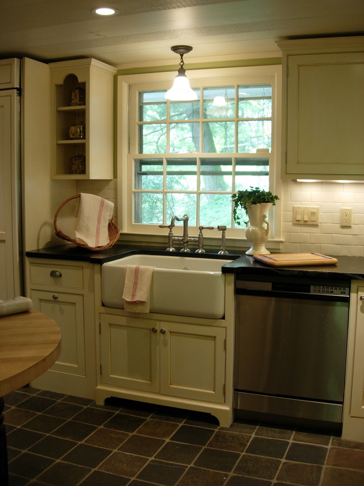 Example of a mid-sized country l-shaped slate floor and gray floor enclosed kitchen design in New York with a farmhouse sink, beaded inset cabinets, white cabinets, soapstone countertops, white backsplash, ceramic backsplash, stainless steel appliances and an island