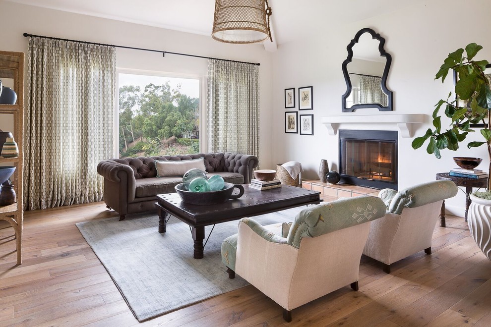 This is an example of a mid-sized beach style formal enclosed living room in Santa Barbara with white walls, medium hardwood floors, a plaster fireplace surround, no tv, beige floor and a standard fireplace.
