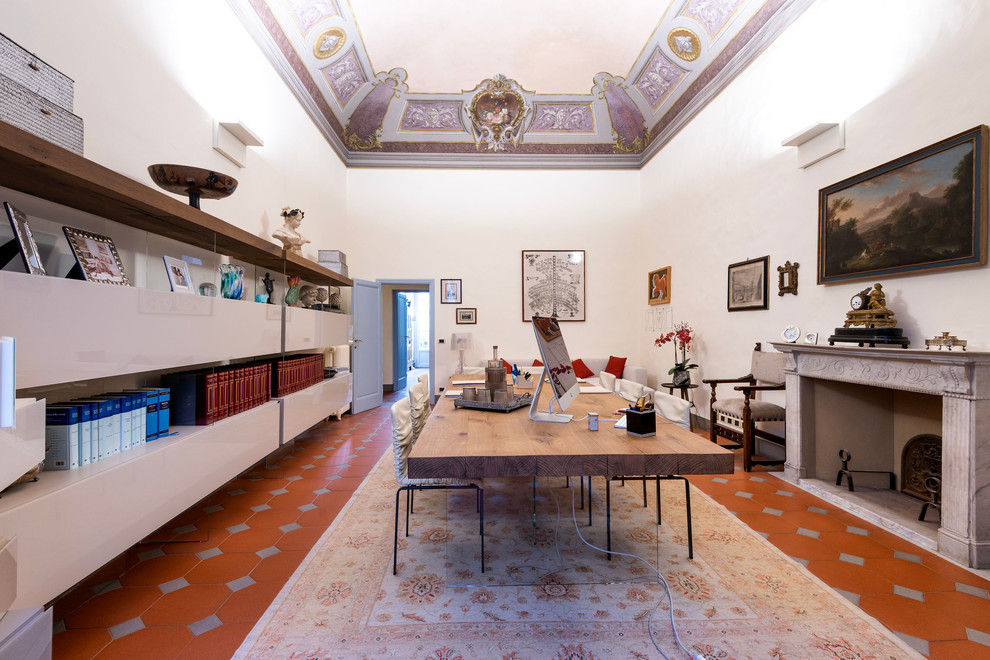 Large modern study room in Florence with white walls, terra-cotta floors, a standard fireplace, a concrete fireplace surround, a freestanding desk and brown floor.