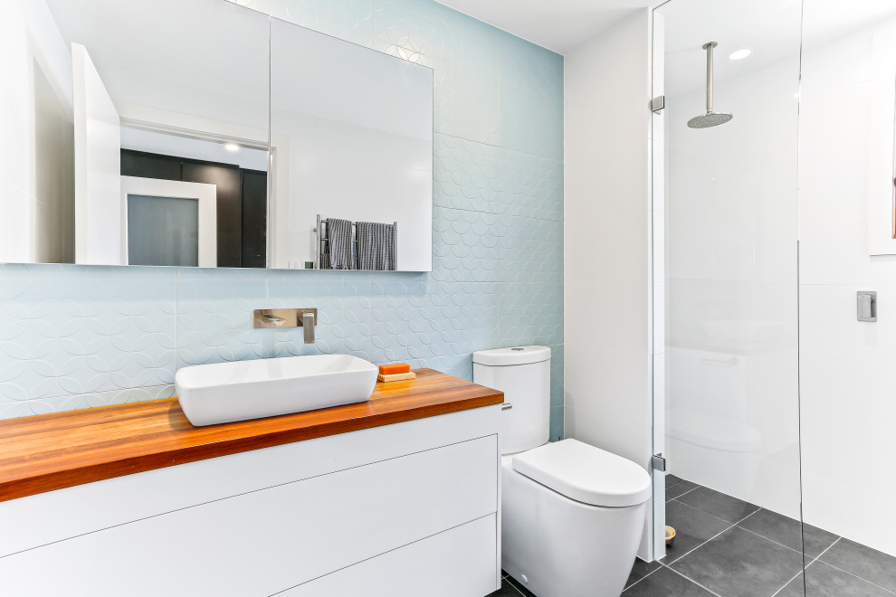 Photo of a contemporary 3/4 bathroom in Central Coast with flat-panel cabinets, white cabinets, a curbless shower, a two-piece toilet, blue tile, white walls, a vessel sink, wood benchtops, grey floor, a hinged shower door and brown benchtops.