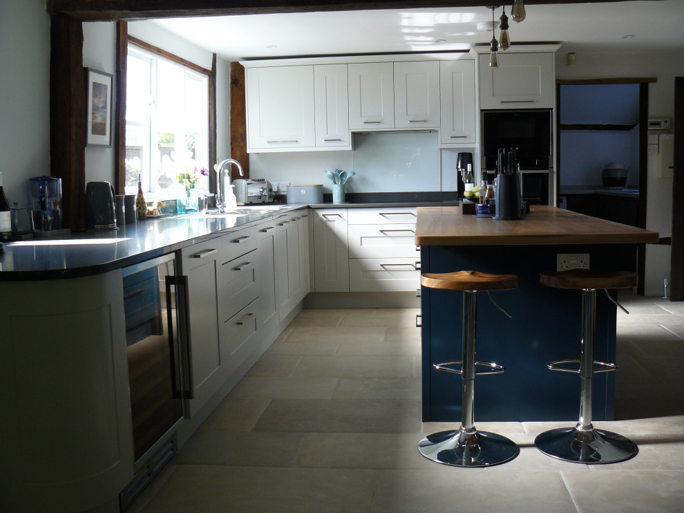 Photo of a large contemporary l-shaped eat-in kitchen in Kent with a double-bowl sink, shaker cabinets, grey cabinets, quartzite benchtops, glass sheet splashback, black appliances, limestone floors, with island, grey floor and grey benchtop.