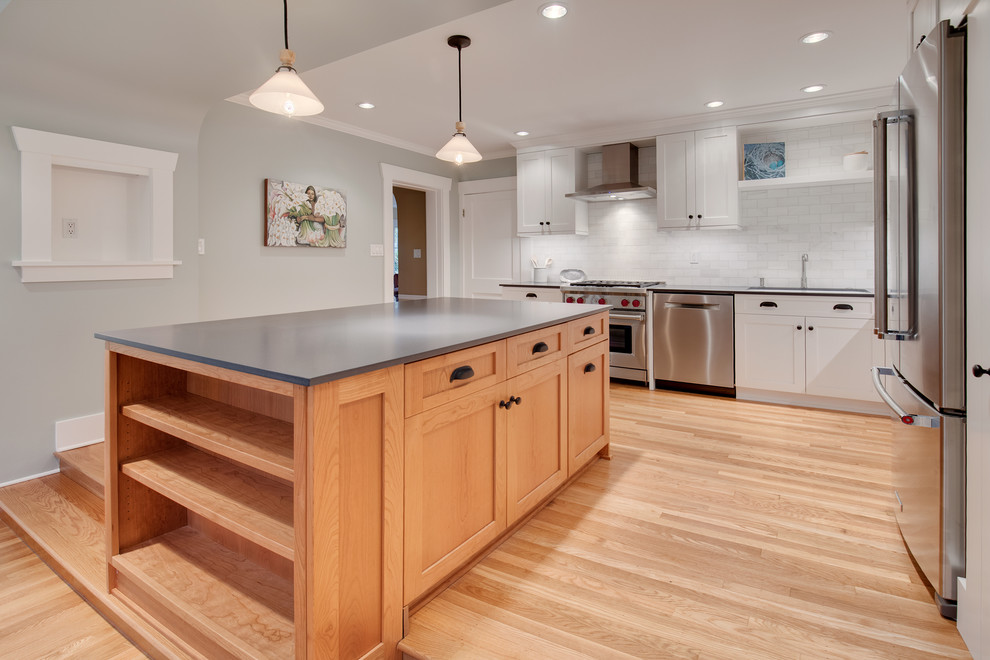 Photo of a mid-sized arts and crafts l-shaped open plan kitchen in Seattle with a drop-in sink, shaker cabinets, white cabinets, quartz benchtops, white splashback, marble splashback, stainless steel appliances, light hardwood floors, with island and brown floor.