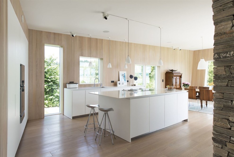 This is an example of a contemporary galley eat-in kitchen in New York with flat-panel cabinets, white cabinets, light hardwood floors and with island.