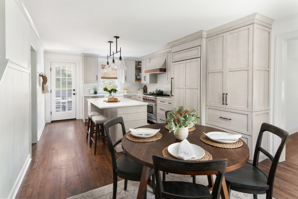 Eat-in kitchen - mid-sized transitional l-shaped medium tone wood floor and brown floor eat-in kitchen idea in New York with a farmhouse sink, shaker cabinets, beige cabinets, quartz countertops, white backsplash, porcelain backsplash, paneled appliances, an island and white countertops