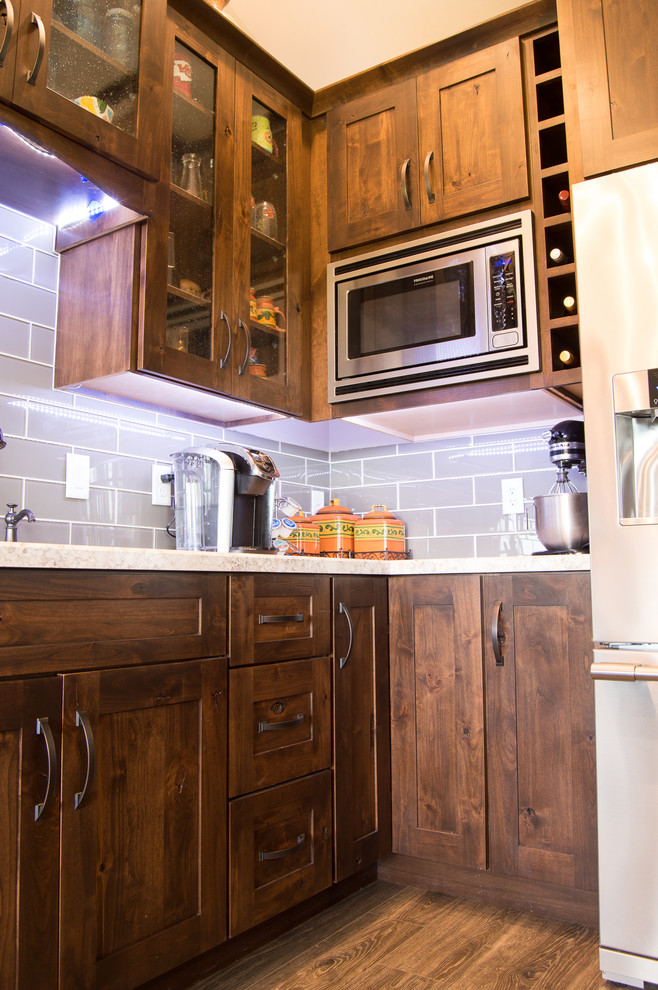 Eat-in kitchen - rustic l-shaped brown floor eat-in kitchen idea with shaker cabinets, brown cabinets, laminate countertops, gray backsplash, stainless steel appliances, an island and beige countertops
