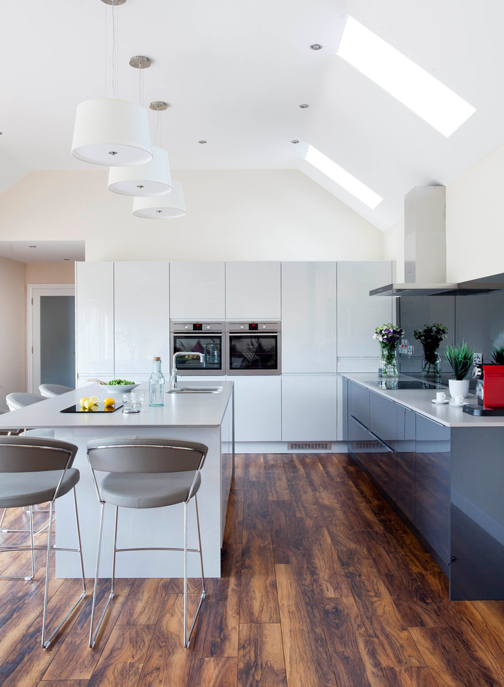 This is an example of a mid-sized contemporary l-shaped open plan kitchen in Other with an integrated sink, flat-panel cabinets, grey cabinets, quartzite benchtops, grey splashback, mirror splashback, stainless steel appliances, medium hardwood floors and with island.