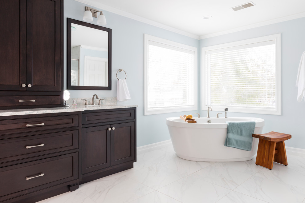 This is an example of a transitional master bathroom in New York with beaded inset cabinets, dark wood cabinets, a freestanding tub, a two-piece toilet, white tile, porcelain tile, blue walls, porcelain floors, an undermount sink and engineered quartz benchtops.