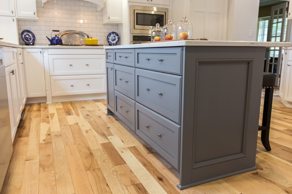 Large transitional u-shaped medium tone wood floor and brown floor enclosed kitchen photo with an undermount sink, shaker cabinets, white cabinets, quartzite countertops, white backsplash, subway tile backsplash, stainless steel appliances and an island