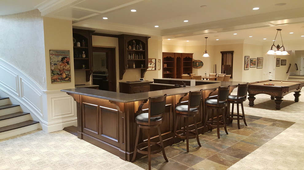 Expansive arts and crafts u-shaped seated home bar in New York with an undermount sink, recessed-panel cabinets, dark wood cabinets, solid surface benchtops, slate floors and multi-coloured floor.
