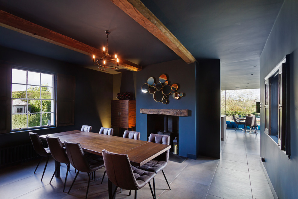 Idée de décoration pour une grande salle à manger ouverte sur le salon design avec un mur bleu, un poêle à bois, un manteau de cheminée en lambris de bois et un sol beige.