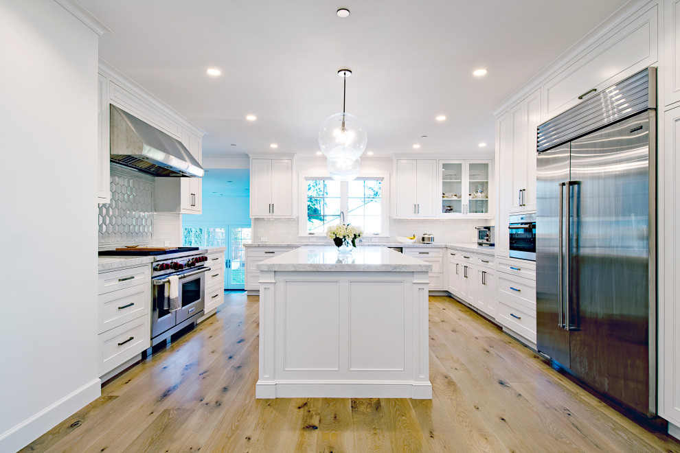 Photo of a transitional u-shaped kitchen in San Francisco with recessed-panel cabinets, white cabinets, stainless steel appliances, medium hardwood floors, with island, brown floor and white benchtop.