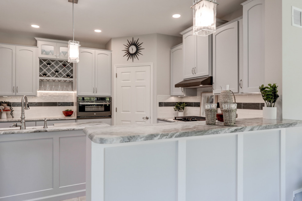 Large transitional l-shaped porcelain tile and gray floor open concept kitchen photo in Other with a farmhouse sink, recessed-panel cabinets, gray cabinets, marble countertops, white backsplash, ceramic backsplash, stainless steel appliances, an island and gray countertops